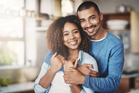 Cheerful couple hugging and smiling in a bright, modern kitchen.